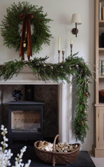 Decorative fireplace mantel with artificial faux greenery, candles, and a basket in a cozy room.