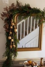 festive faux foliage draped on mirror with large brass cowbells on a garland 