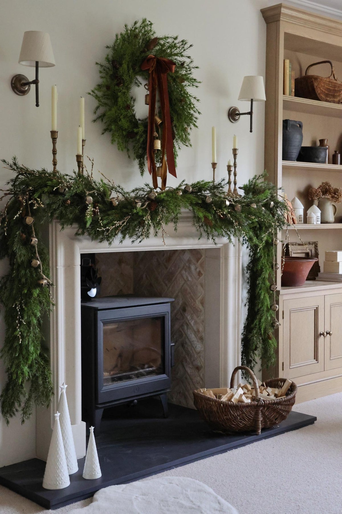 Decorative fireplace mantel with artificial faux garlands and wreath, candles, and abells in a cozy living room.