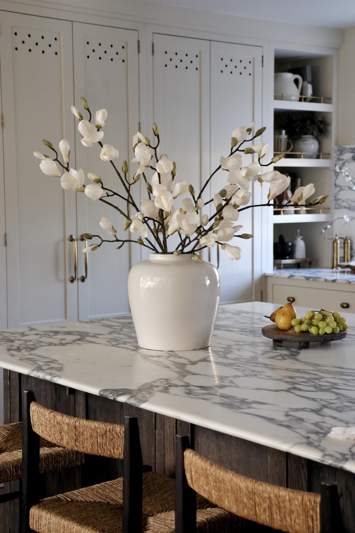 tall faux white magnolia branches in ceramic white vase on a marble topped kitchen island 
