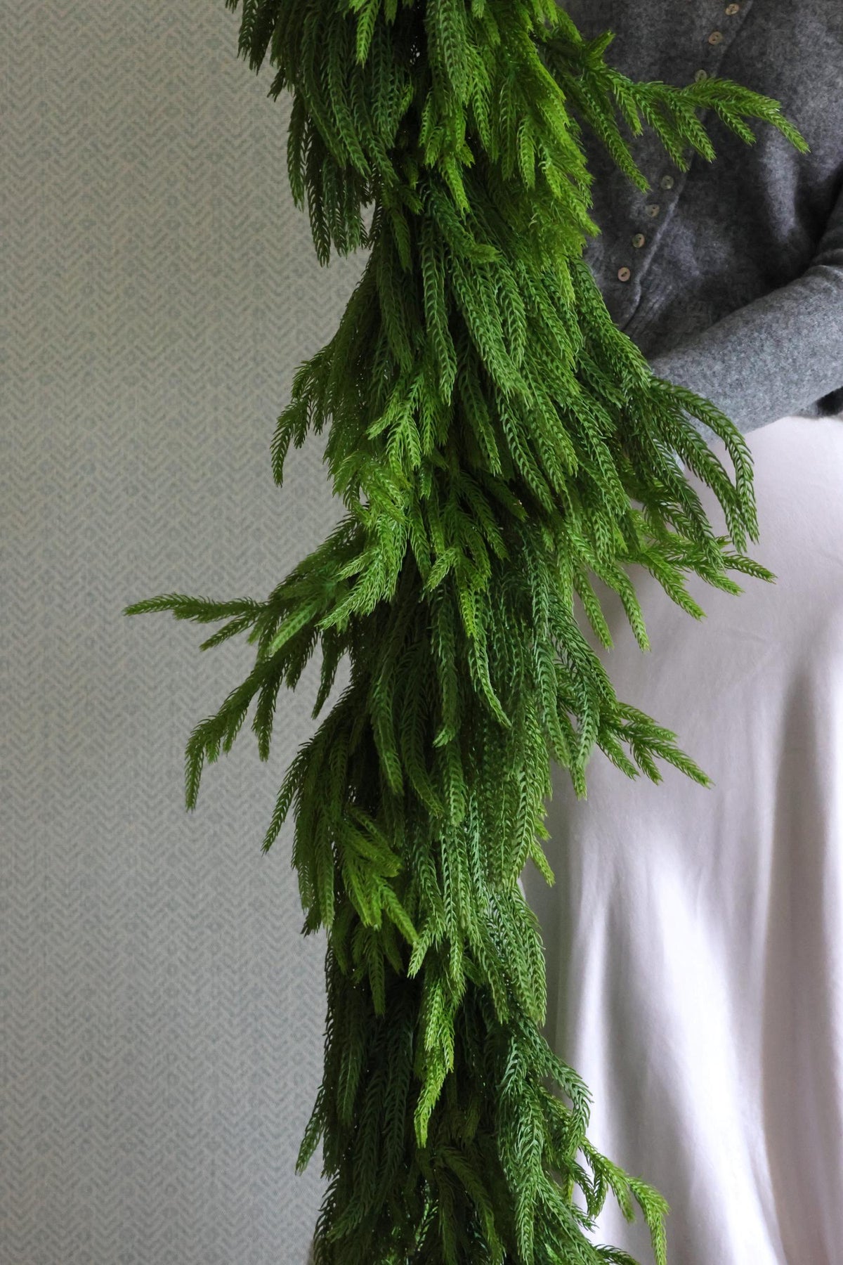 Green artificial garland draped over a person wearing a gray shirt and white pants.