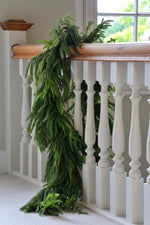Green norfolk pine garland draped over a wooden railing with a white staircase in the background