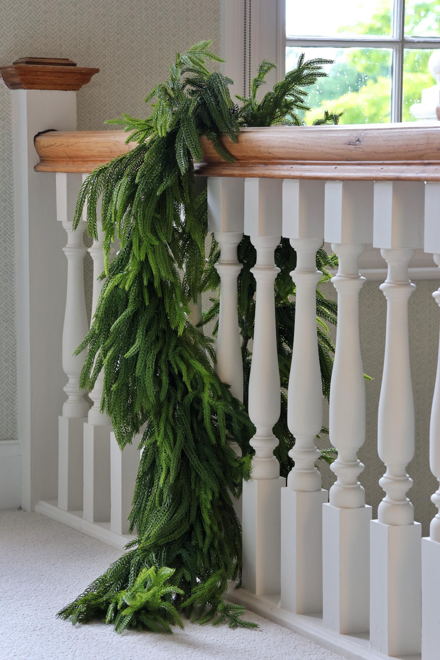 Green norfolk pine garland draped over a wooden railing with a white staircase in the background