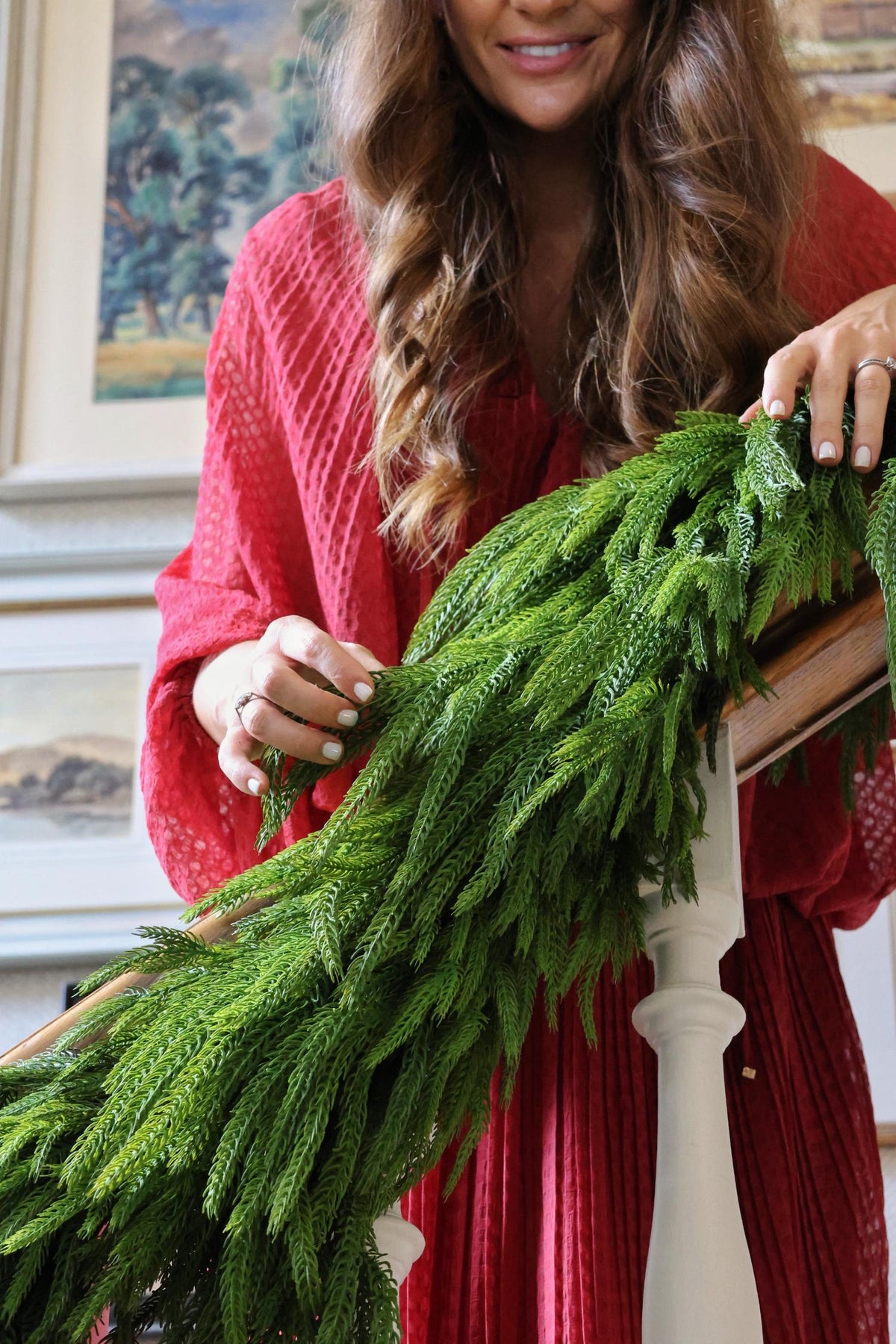 Woman holding fixing a faux norfolk pine garland to a staircase 