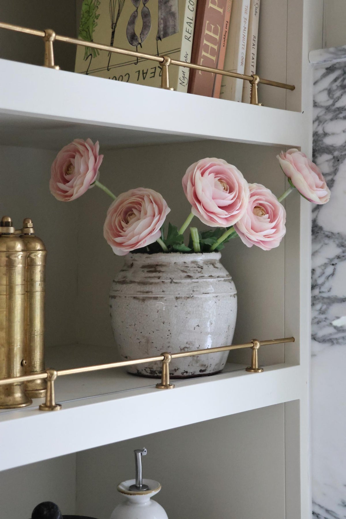 pink ranunuclus flower in a white vase on beige shelving