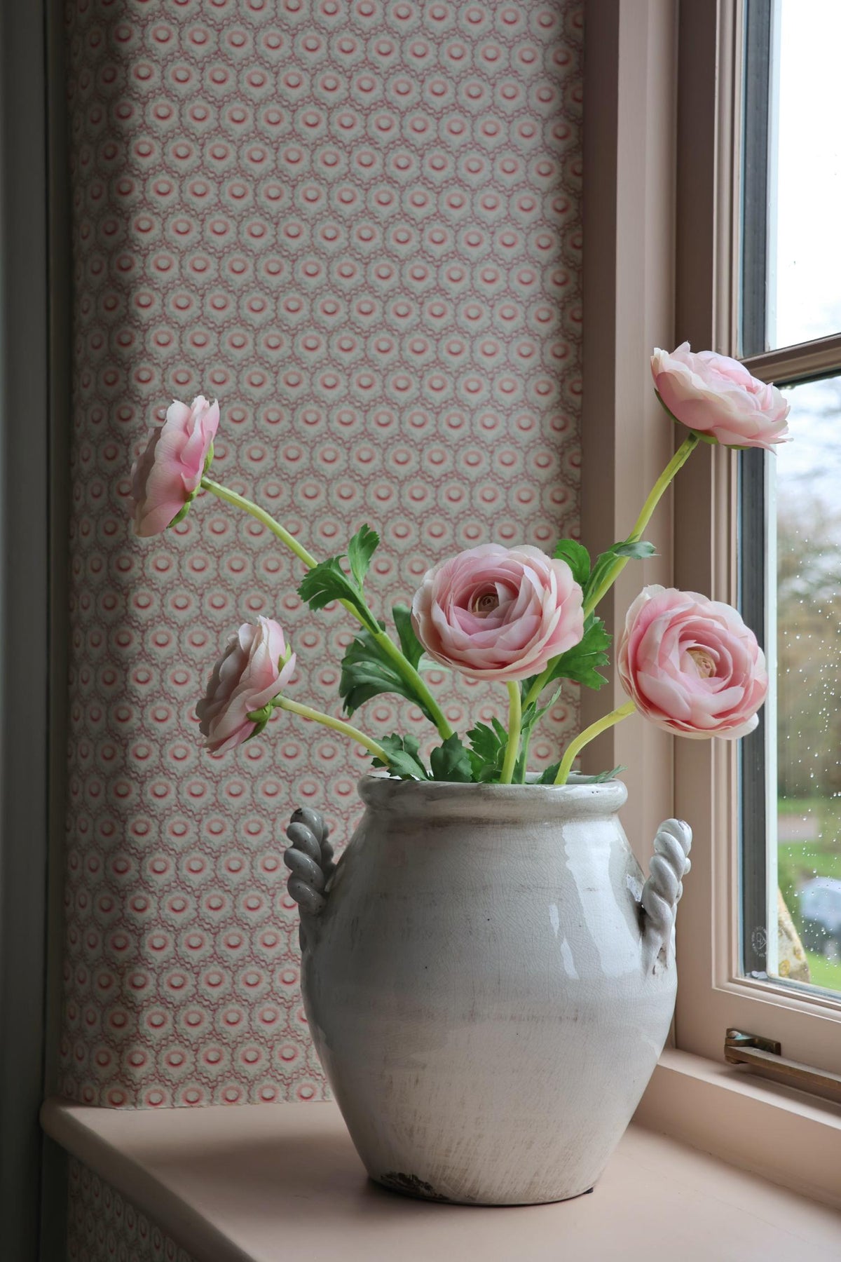 white vase on windowsill with pink ranunculus flower in