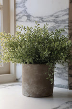 A faux potted Eucalyptus bush with green leaves, placed in a rustic grey stone pot.