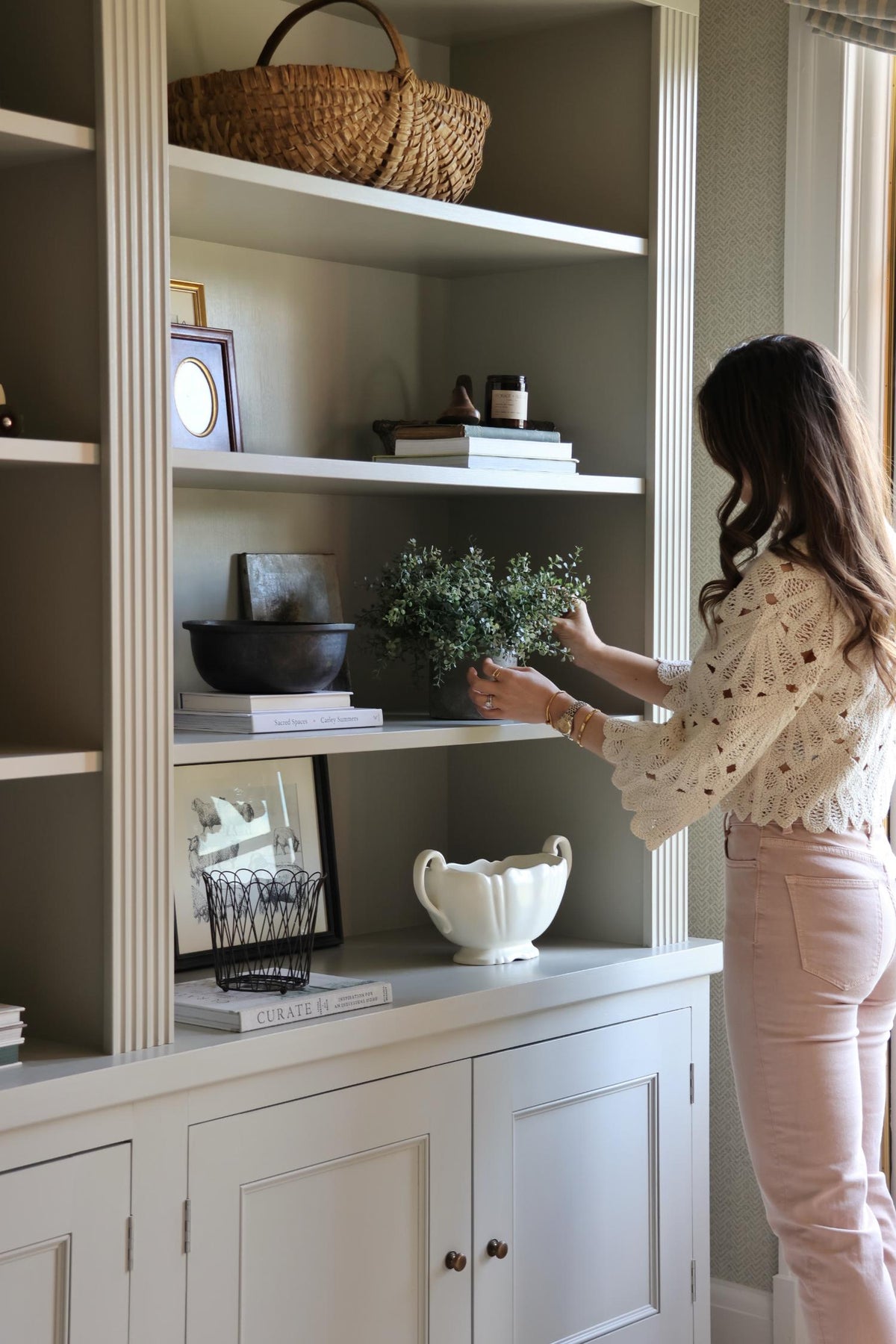 faux potted eucalyptus bush plant being arranged on cabinetry by a lady in pink jeans and beige top 
