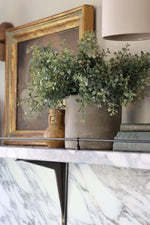 faux potted eucalyptus bush plant on marble shelf with black brackets and rail 
