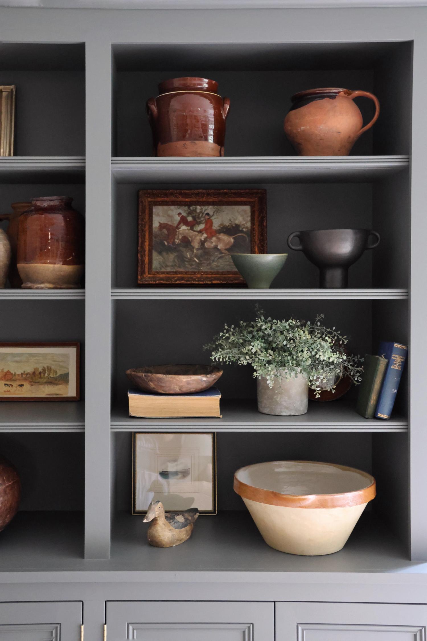 faux potted eucalyptus bush plant on dark blue shelving with other decorative items 