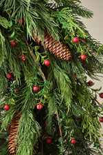 close up of artificial green foliage with scattered red berries and pinecones 