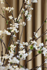 Artificial white sakura blossom flowers on branches against a beige curtain background