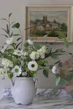 Floral arrangement in a white vase on a marble surface with a framed painting in the background.