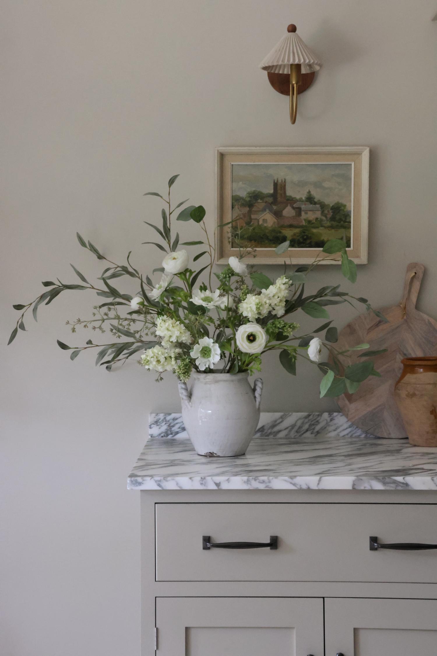 Floral arrangement in a white vase on a marble surface with a painting in the background.