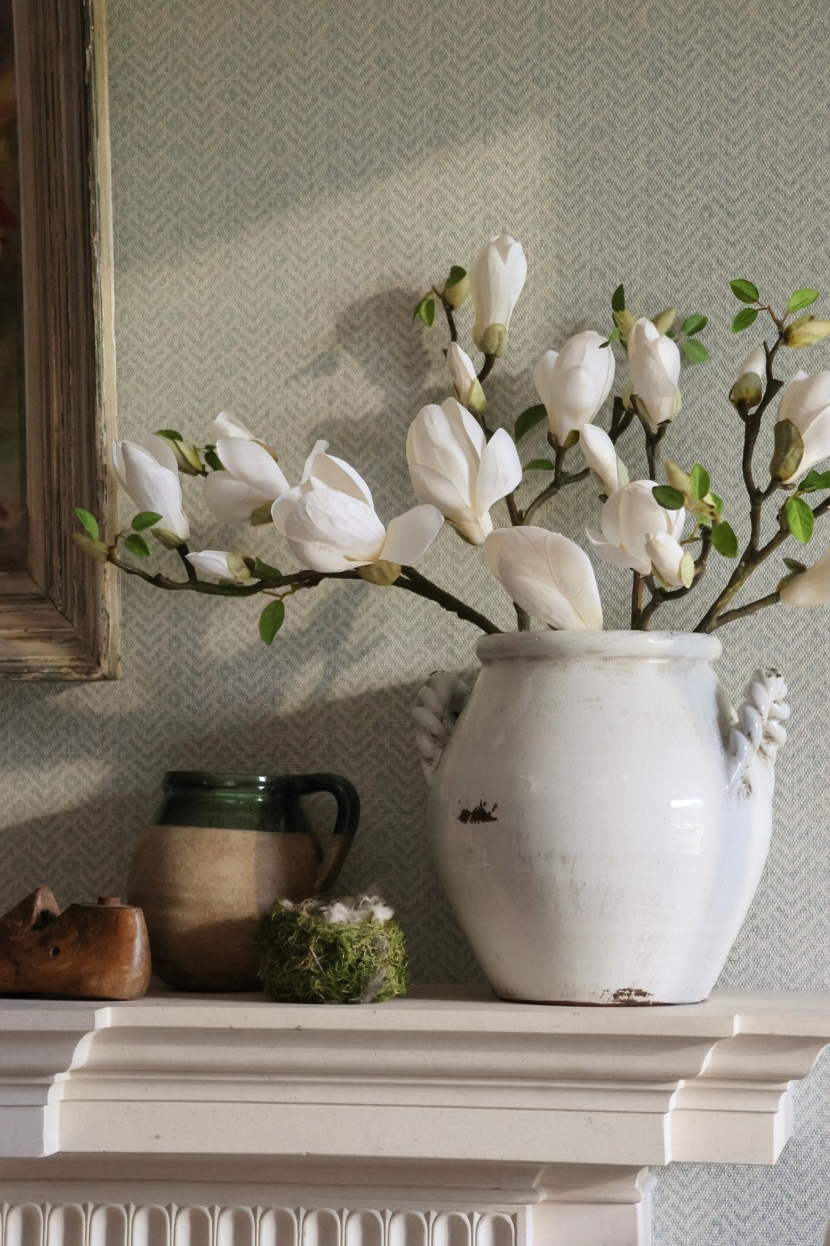 White vase with magnolia flower on a mantelpiece against a textured wall.