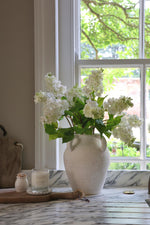 white stone vase on marble surface with faux white lilac stems in