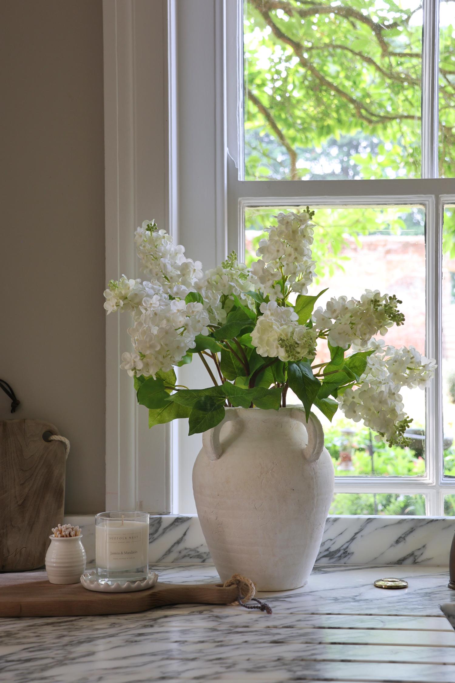 white stone vase on marble surface with faux white lilac stems in