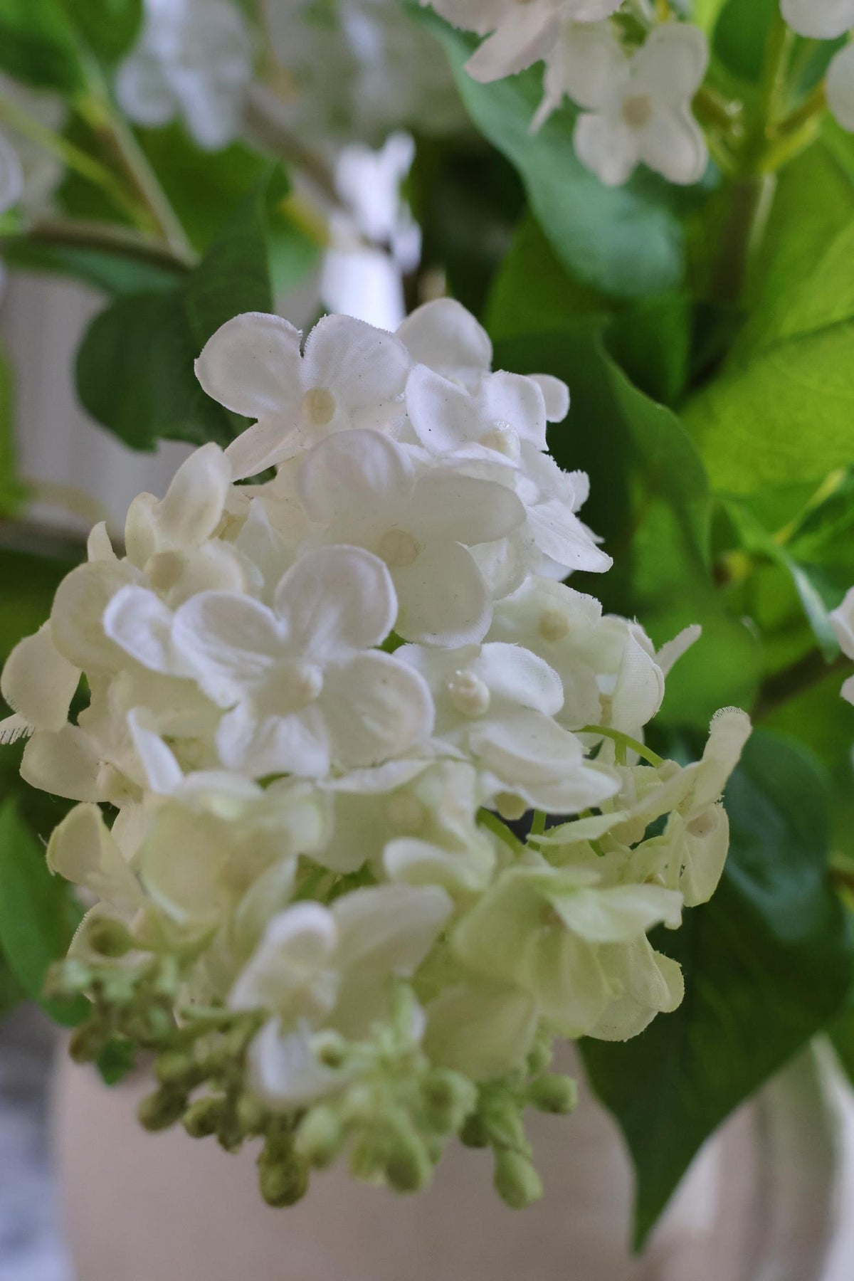 faux white lilac spray close up of white petals and green leaves 