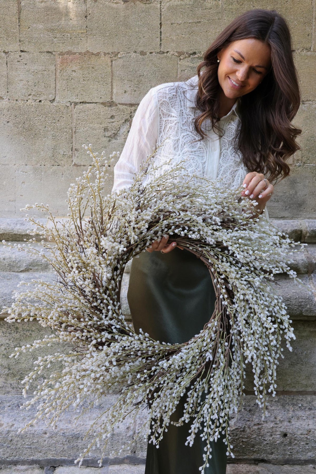 A person holding a faux white willow wreath against a stone wall background.