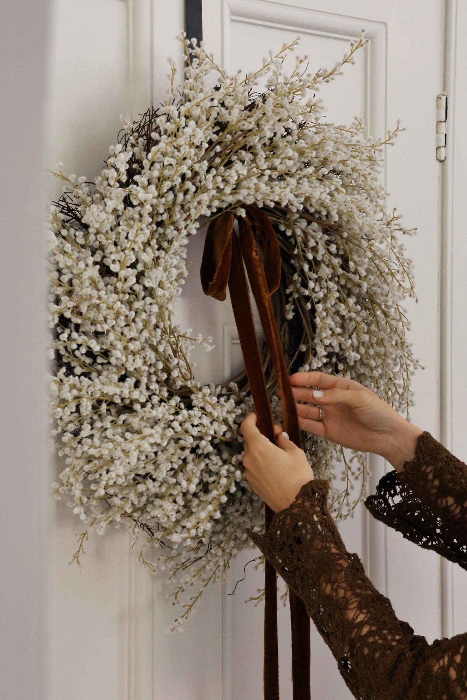 faux white willow wreath with dark brown velvet ribbon hanging on a white door 