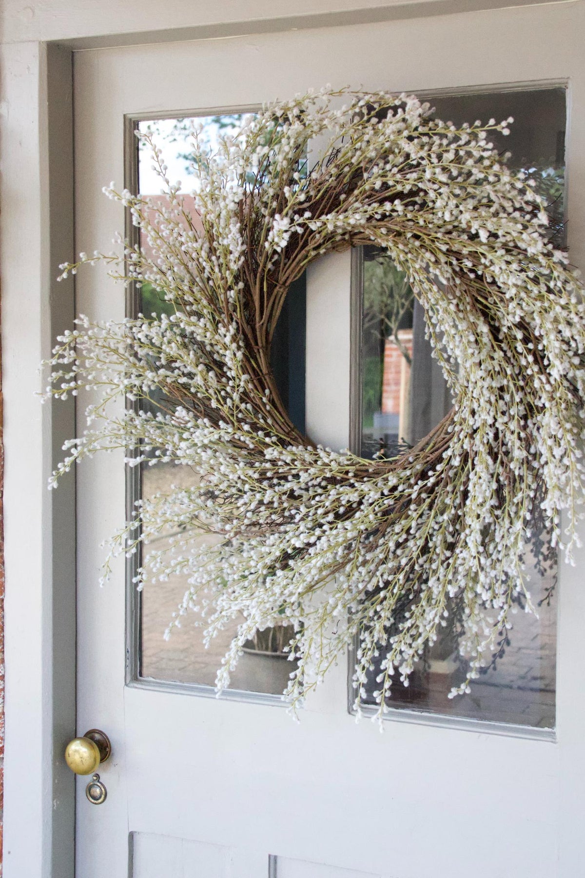 faux white willow wreath hanging on a pale blue door with glass panels and brass door knob