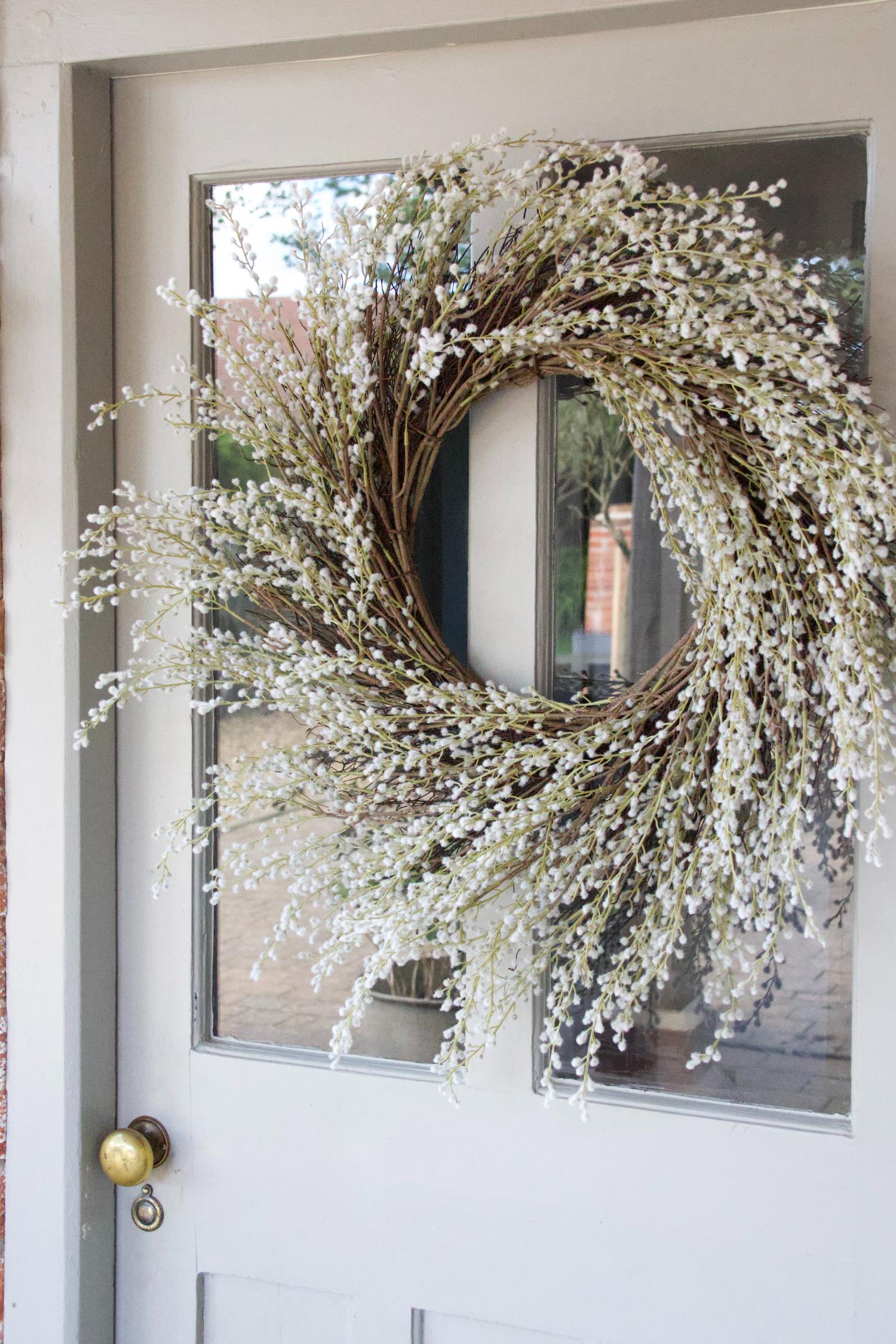 faux white willow wreath hanging on a pale blue door with glass panels and brass door knob