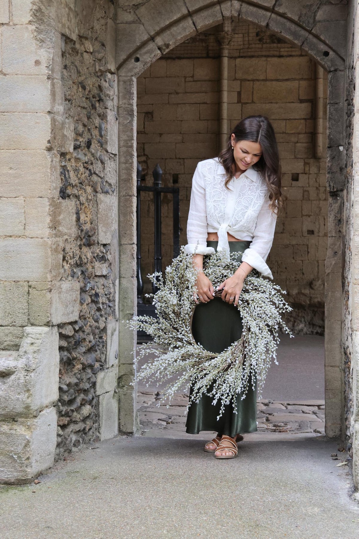 lady standing under archway holding artificial white willow wreath