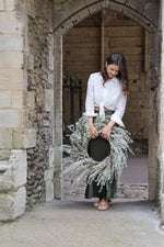 lady standing under archway holding artificial white willow wreath