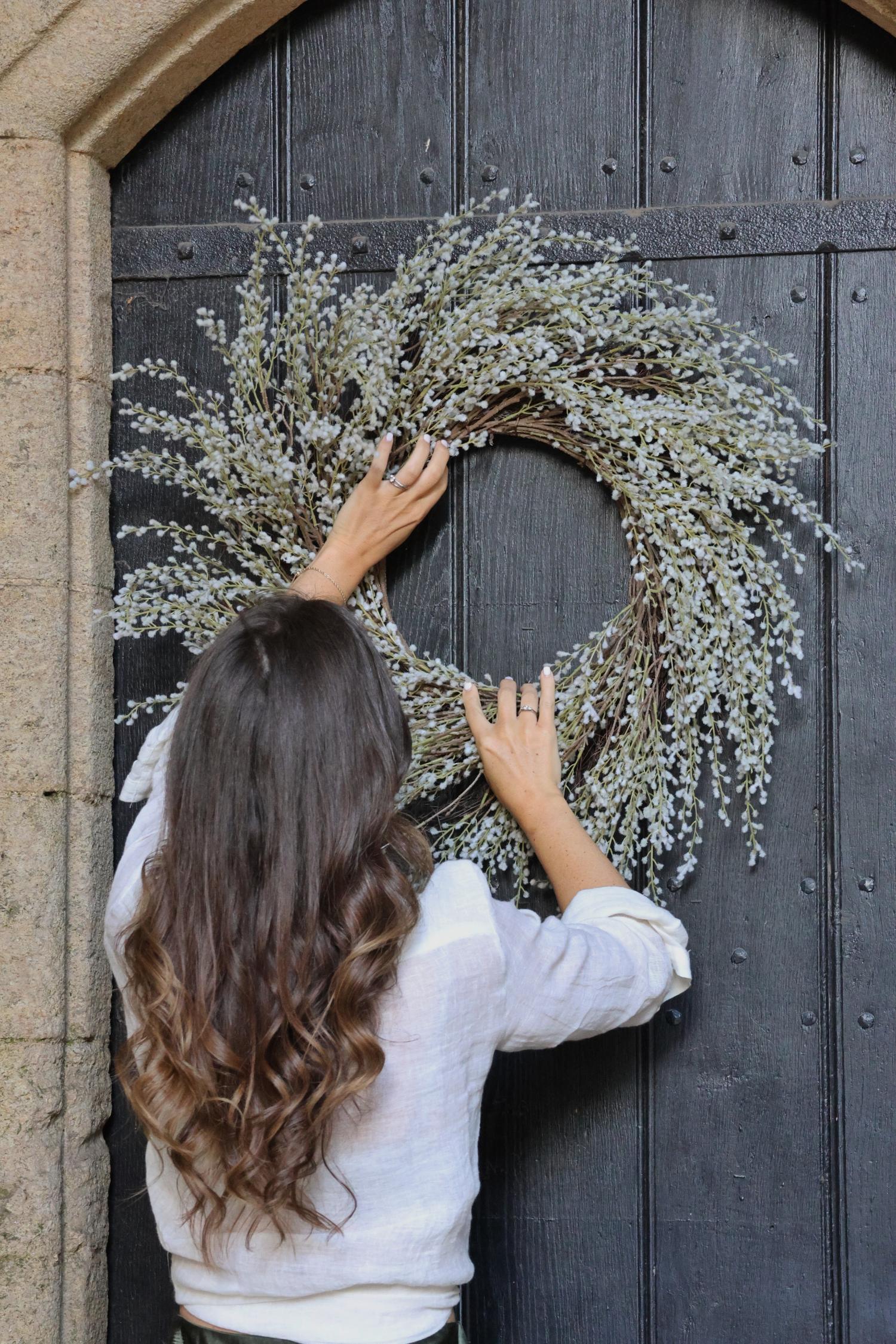 faux white willow wreath on a dark brown door and women holding it in position