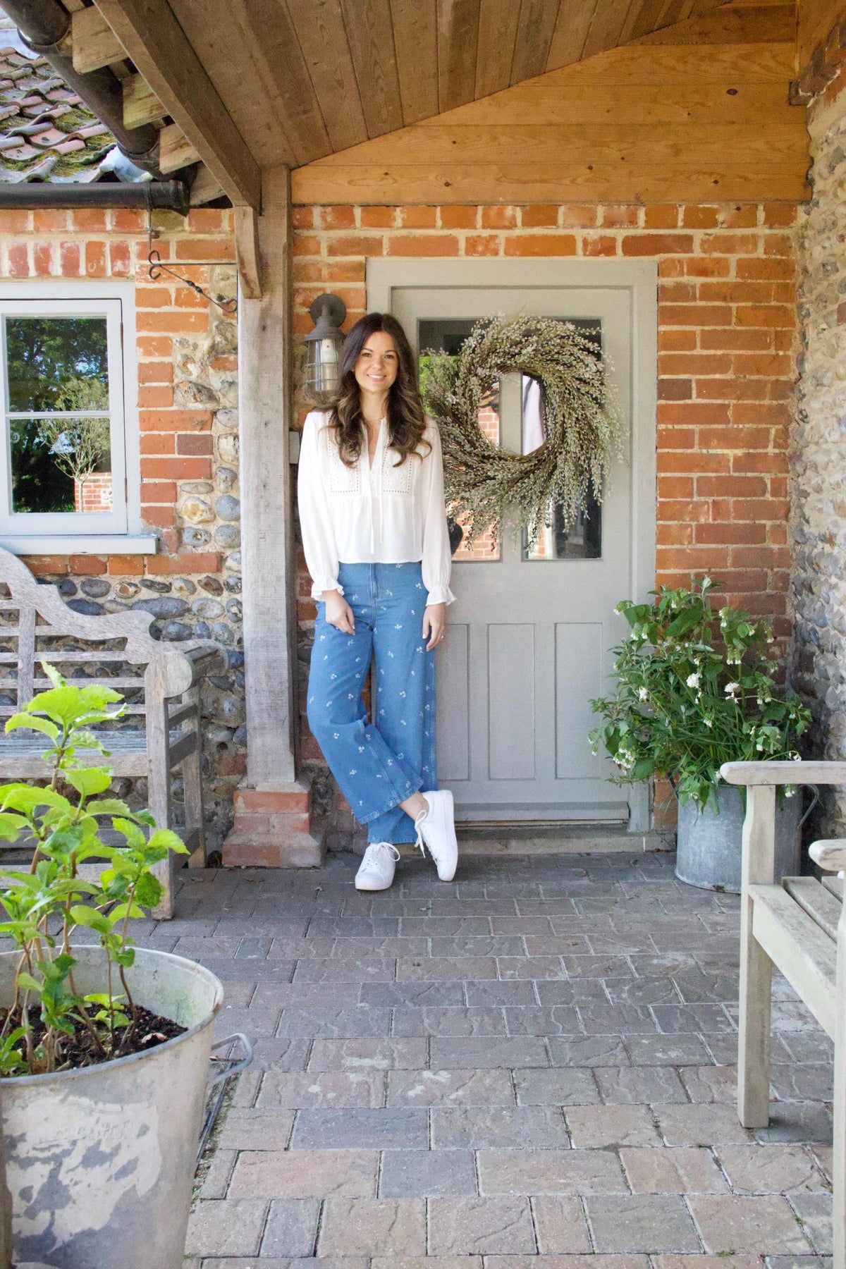 lady standing infront of a cottage with faux white willow wreath hanging on the door 