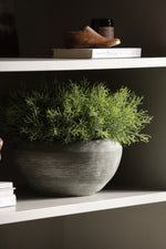 Gray vase with green faux spanish moss on a white shelf against a dark wall