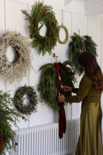 artificial christmas wreaths on a large white wall with women arranging ribbon on one of them 