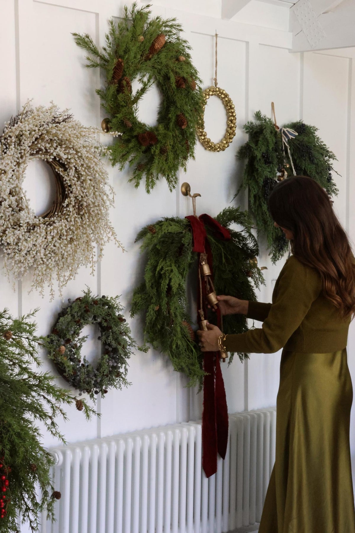 artificial christmas wreaths on a large white wall with women arranging ribbon on one of them 