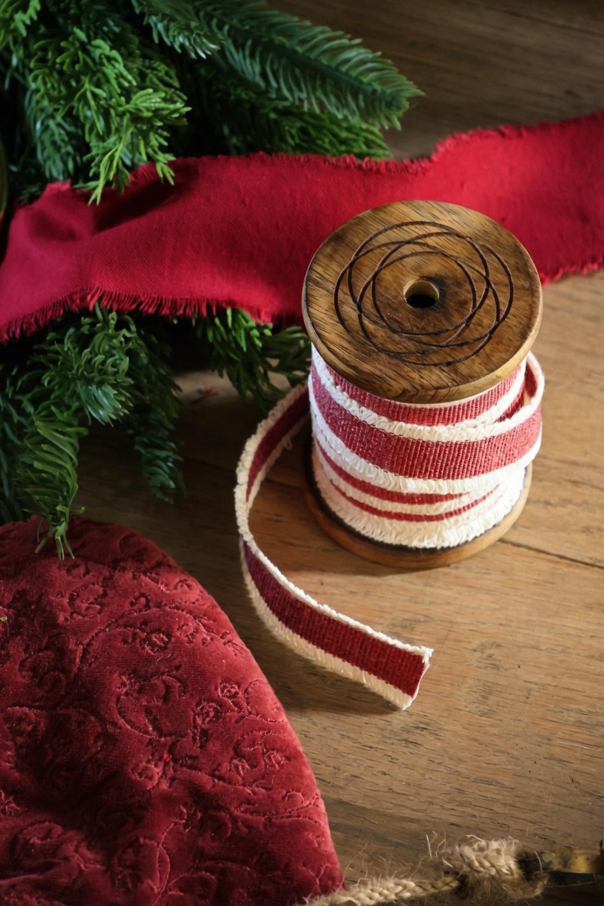 red ribbon on wooden spool with foliage on a wooden surface 