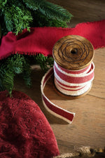 red ribbon on wooden spool with foliage on a wooden surface 