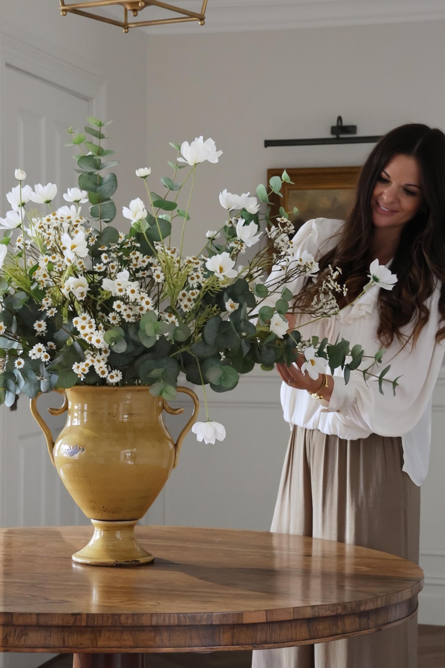 Woman arranging flowers in a yellow vase on a wooden table