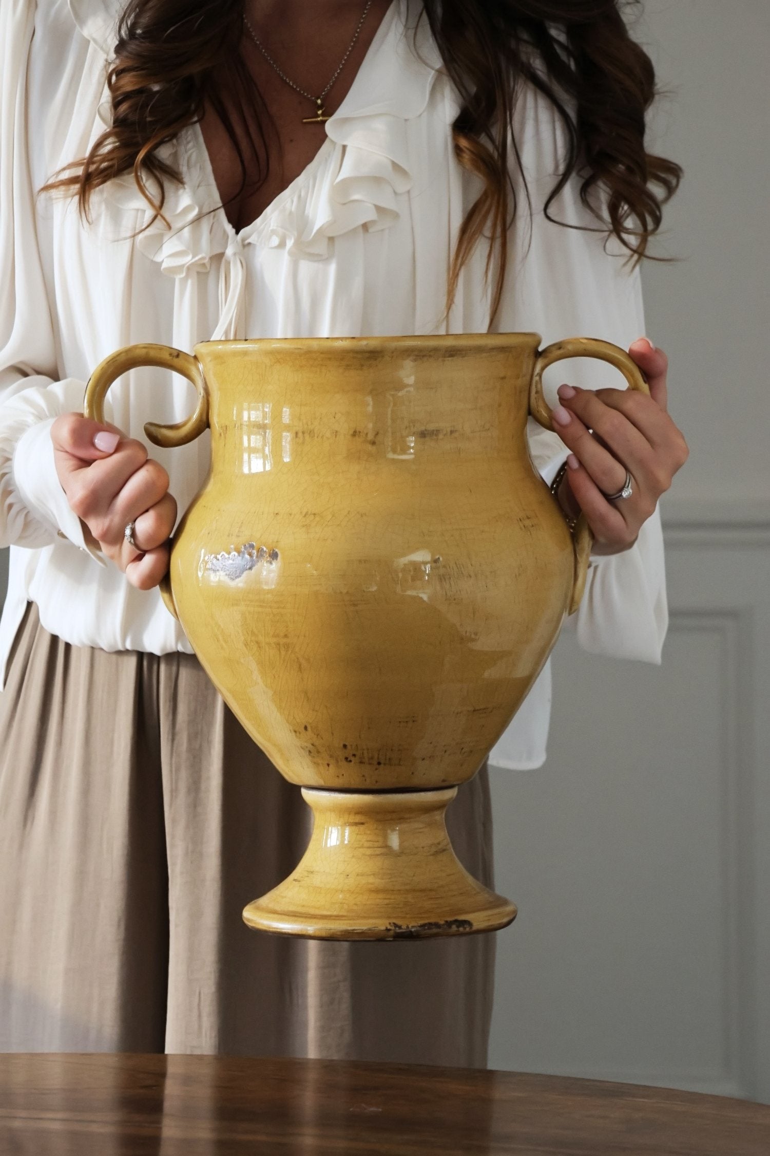 Person holding a large yellow ceramic vase indoors
