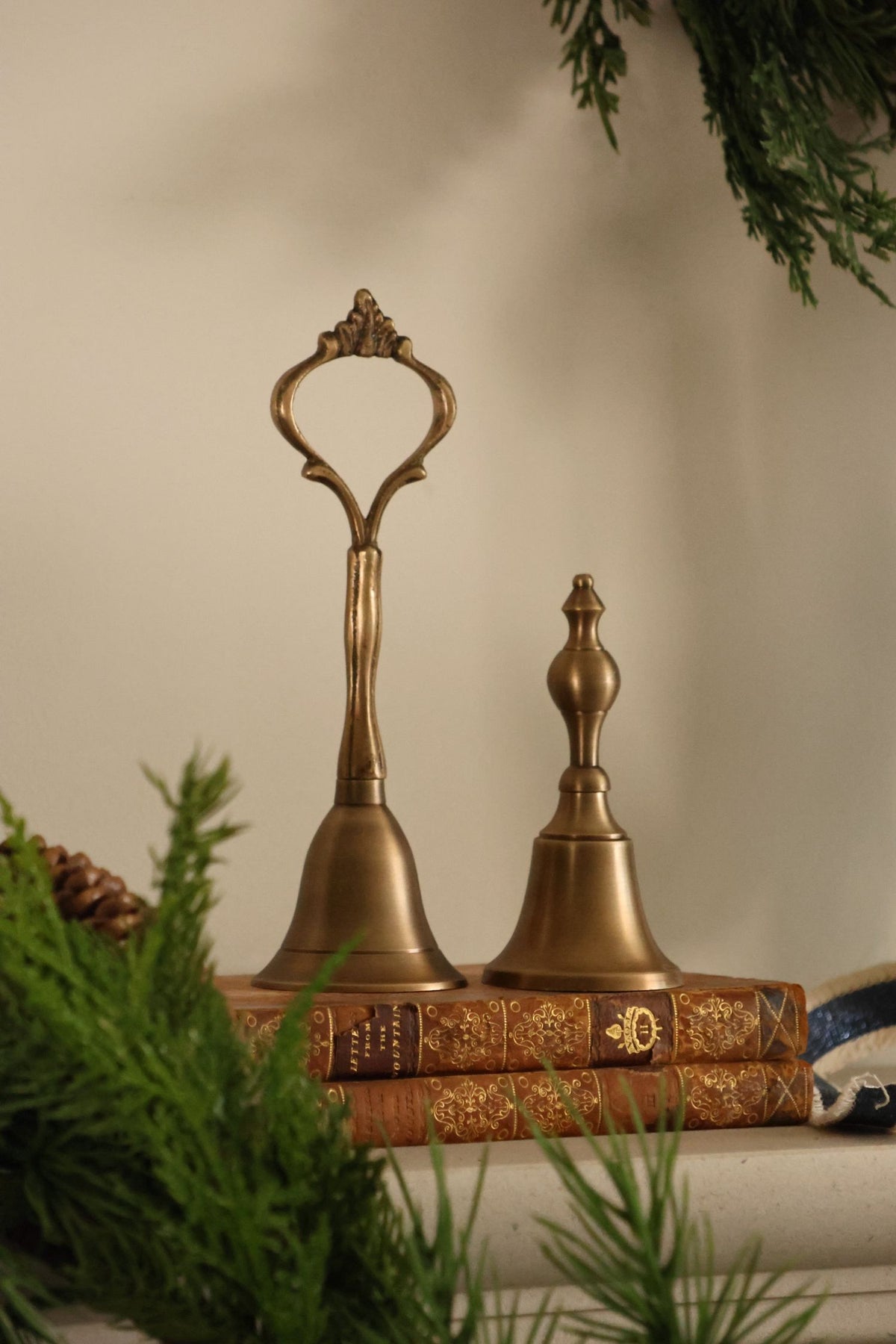 two brass bells sat ontop of  brown vintage books on a plain background 
