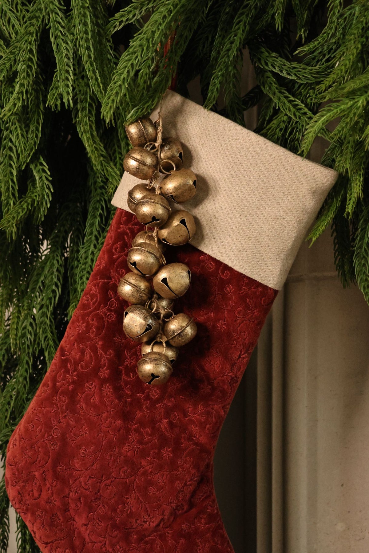 small brass bells clustered and hanging from a red stocking with artificial norfolk pine garland above it 
