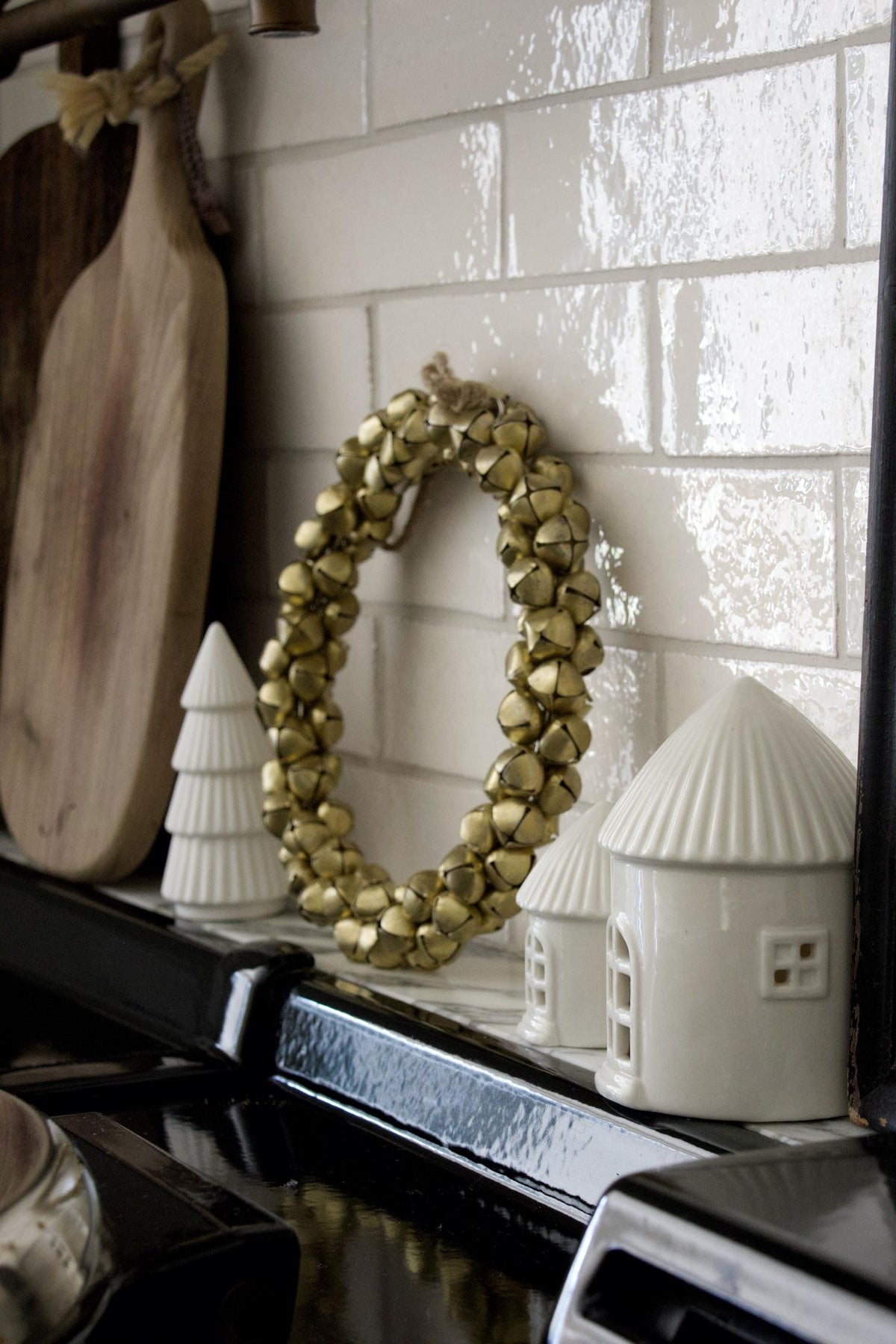 Decorative items including a gold bell wreath, white ceramic trees, and a white ceramic house on a shelf.