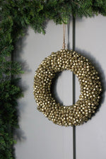 A large round wreath made up of golden jingle bells, hanging outdoors with a jute string.