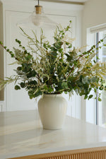 White vase with greenery on a white surface in a bright room