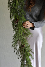 Person holding a faux green garland against a neutral background