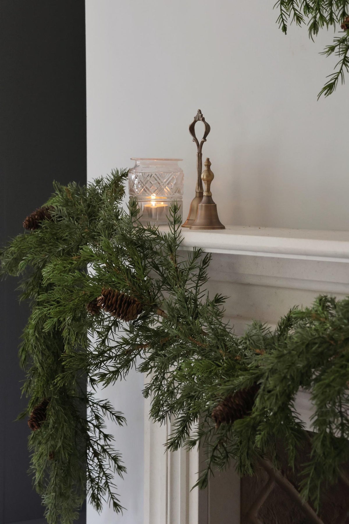 Decorative artificial garland with a candle and bell on a mantelpiece.