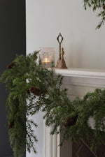 Decorative artificial garland with a candle and bell on a mantelpiece.