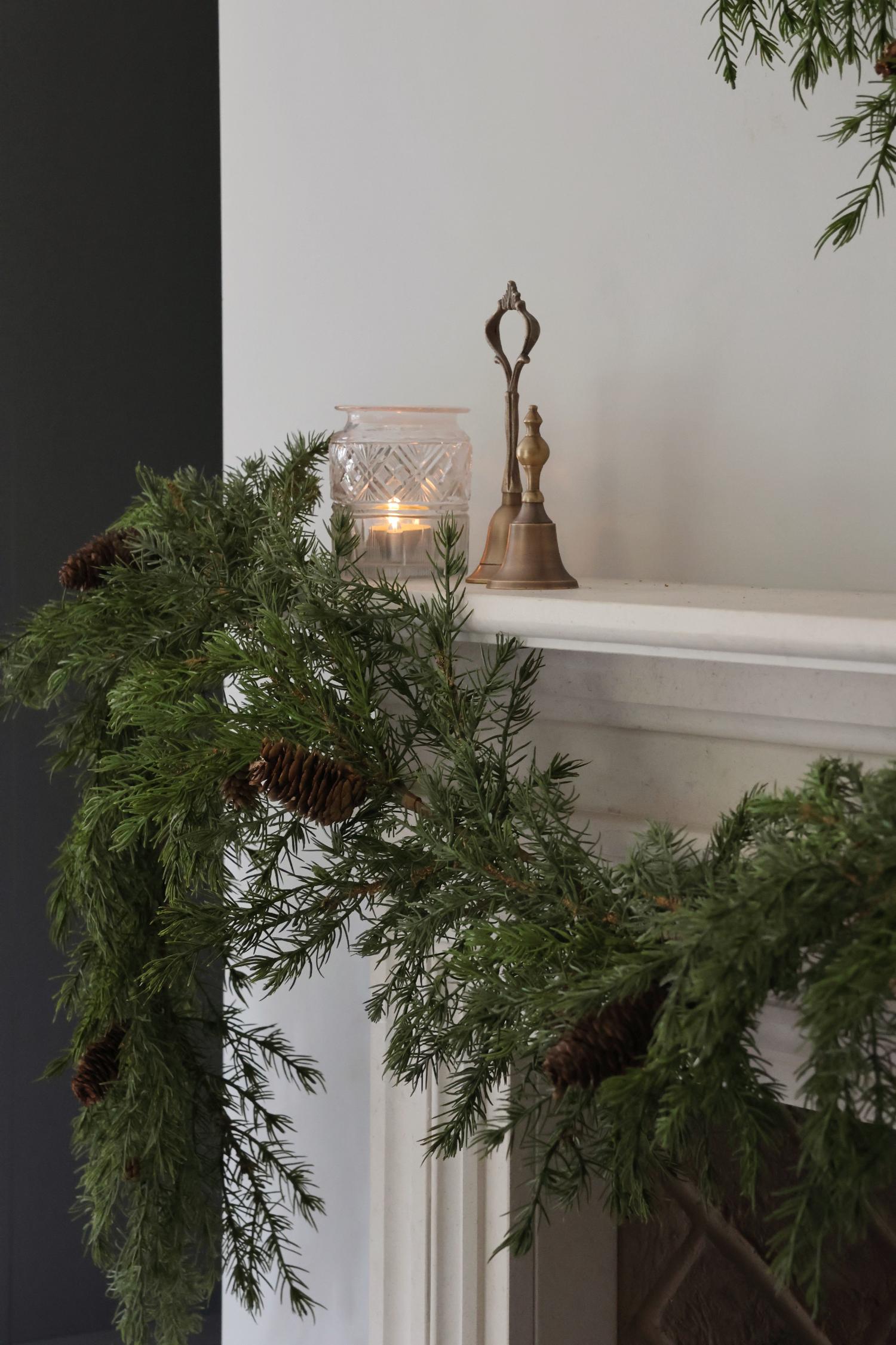 Decorative artificial garland with a candle and bell on a mantelpiece.