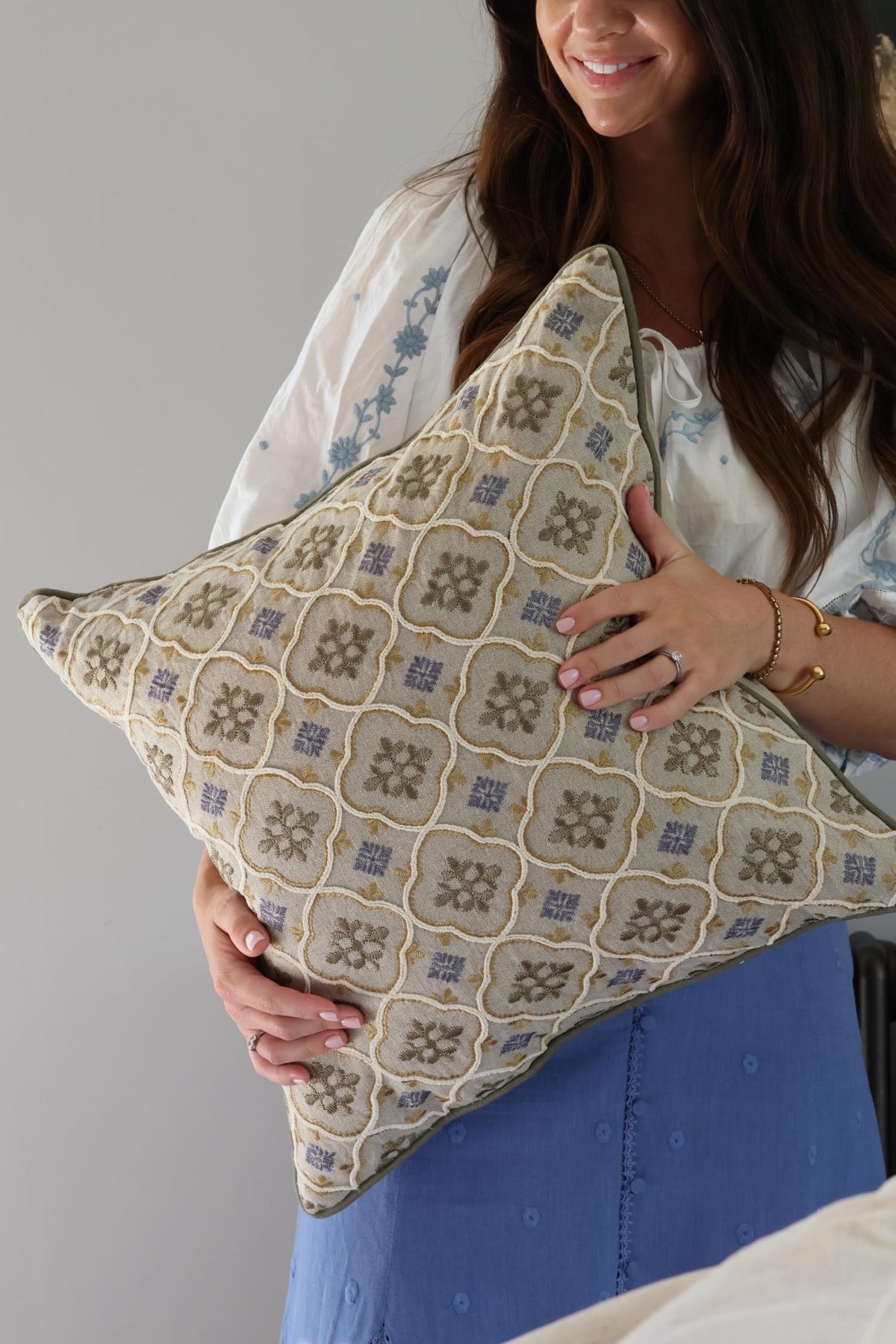 Woman holding a decorative cushion with a geometric pattern against a neutral background