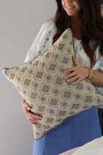 Woman holding a decorative cushion with a geometric pattern against a neutral background
