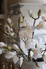 White faux magnolia branches in a vase with a blurred background