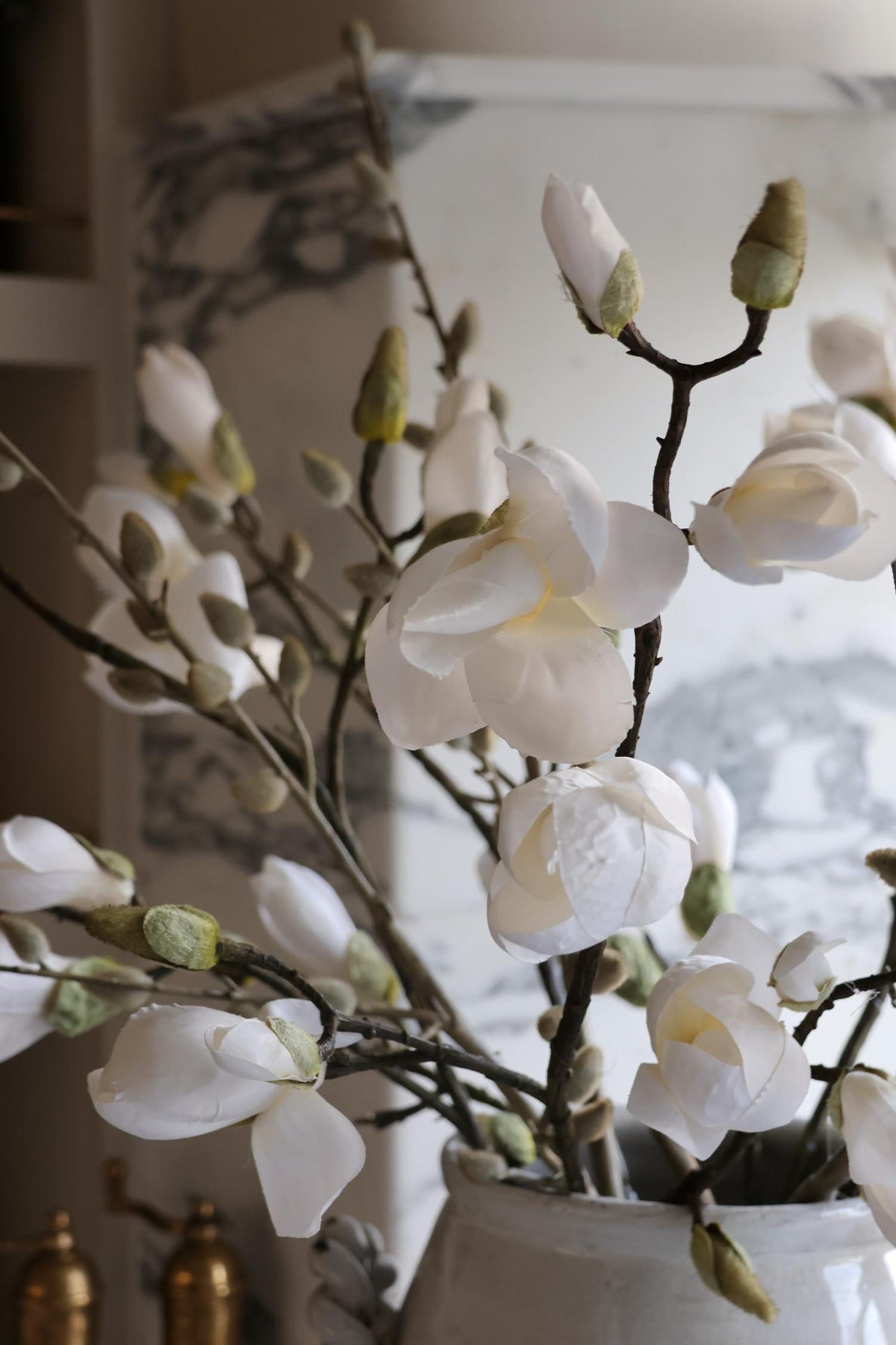 White faux magnolia branches in a vase with a blurred background